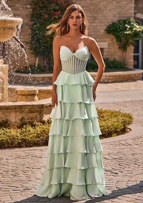Woman in sage green sweetheart neckline gown with layered ruffled skirt standing in courtyard near fountain