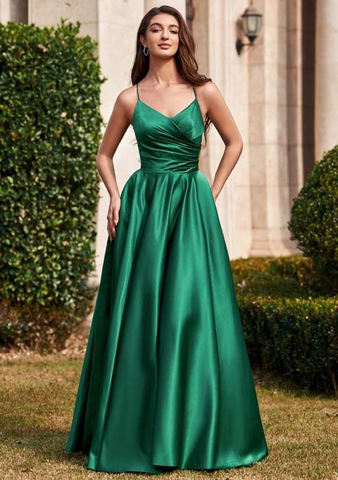 Woman in emerald green satin gown with V-neckline standing in front of elegant mansion with manicured hedges